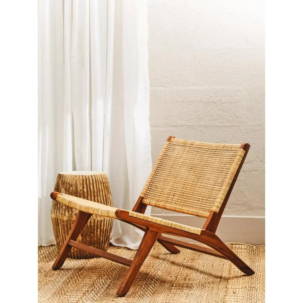 rattan lounge chair with wooden frame on woven rug beside textured side table in bright room