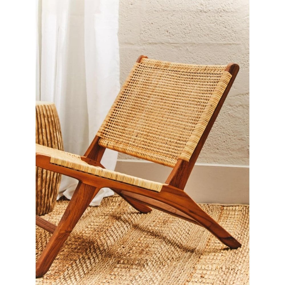 Natural rattan lounge chair with wooden frame on woven rug in modern living space