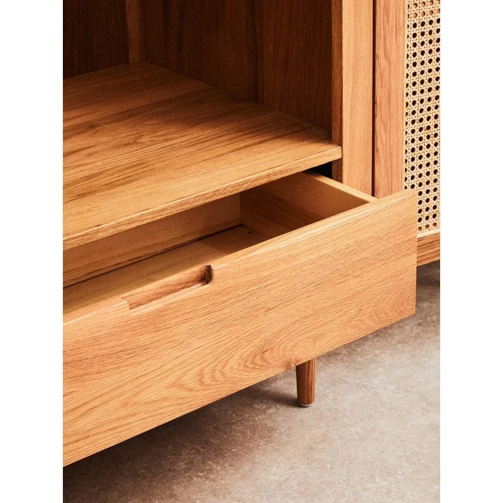 Oak sideboard with open drawer and rattan panel on concrete floor