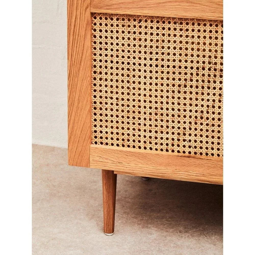 Close-up of wooden sideboard with woven cane panel and tapered leg on stone floor