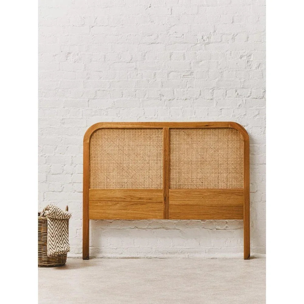 Rattan and oak headboard against white brick wall with woven storage basket nearby