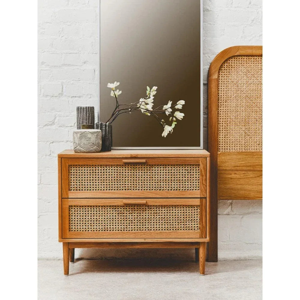Wooden bedside table with rattan drawers, ceramic vases, flowers, and mirror