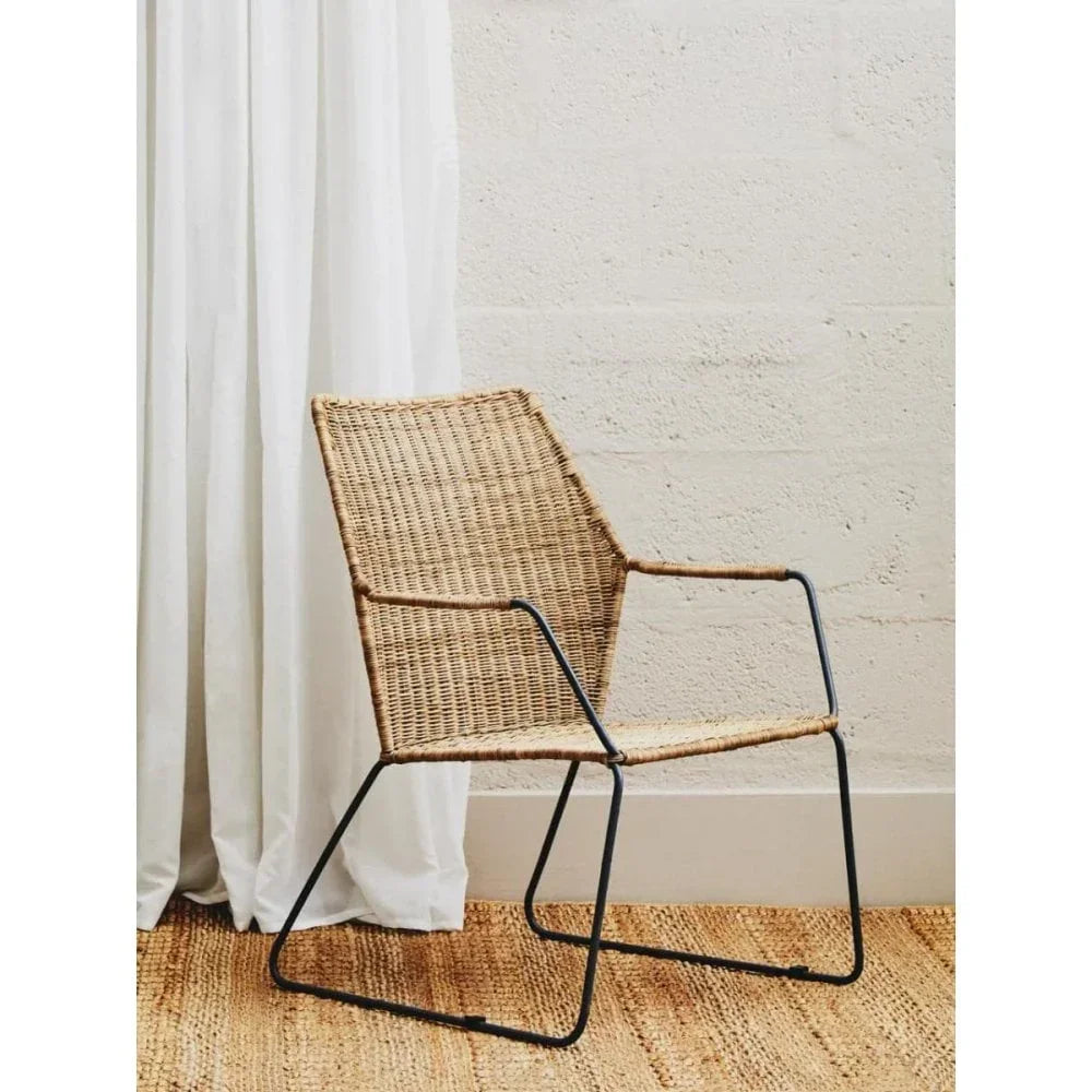 Rattan dining chair with black metal legs next to white curtain and textured wall