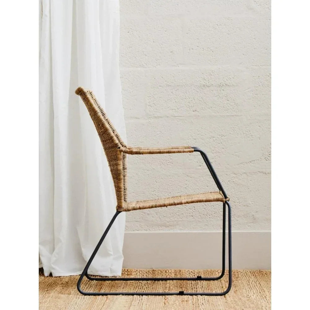 Modern rattan dining chair with black metal frame on natural woven rug
