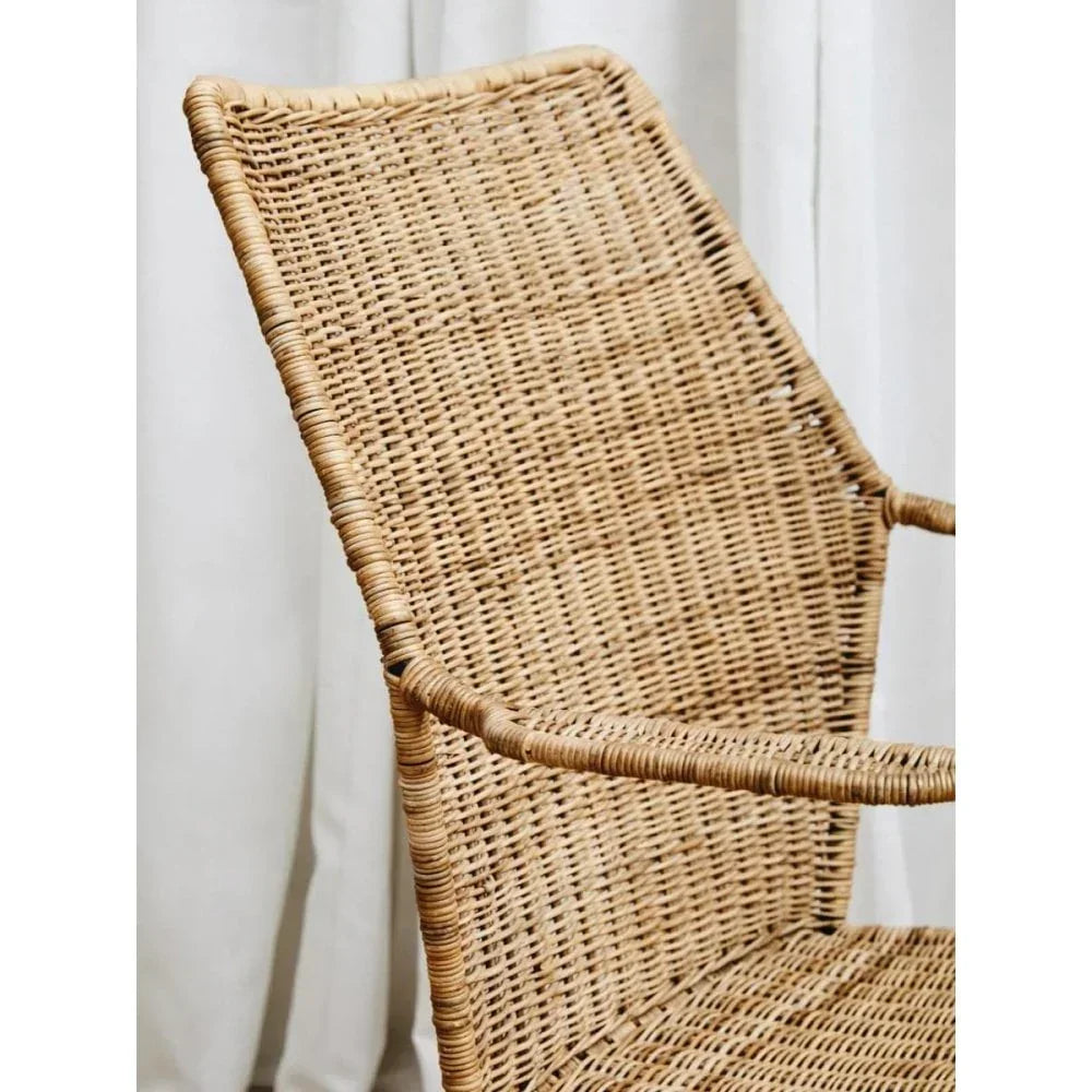 Natural rattan dining chair with high backrest and armrests against a white curtain backdrop