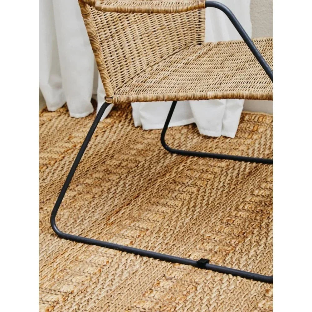 Woven rattan chair with black metal frame on natural jute rug beside white curtain