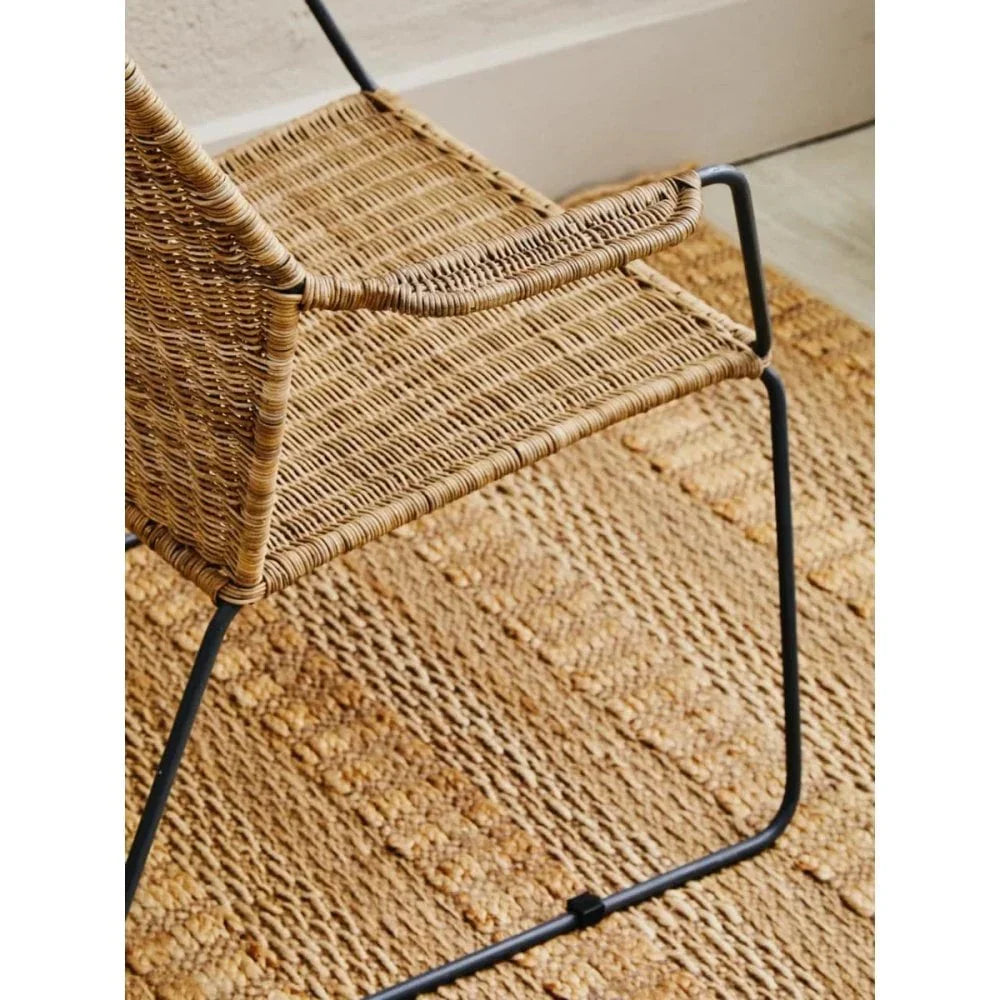 Woven rattan dining chair with black metal frame on textured natural rug