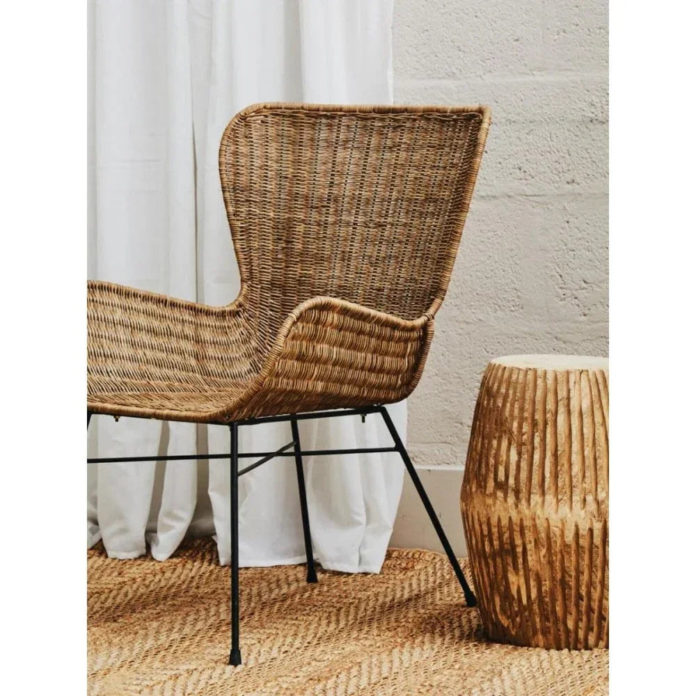 Natural rattan wingback chair with black metal legs beside textured wooden side table