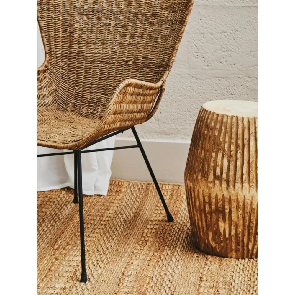 Wicker accent chair with black legs beside carved wooden side table on woven rug