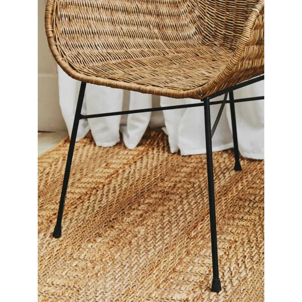 Wicker dining chair with black metal legs on woven jute rug