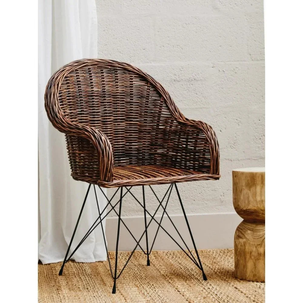 Brown rattan armchair with black metal legs on woven rug beside wooden accent table