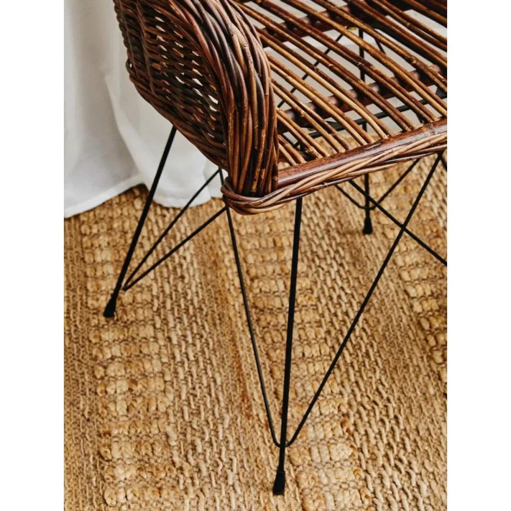Brown rattan dining chair with black metal legs on woven jute rug