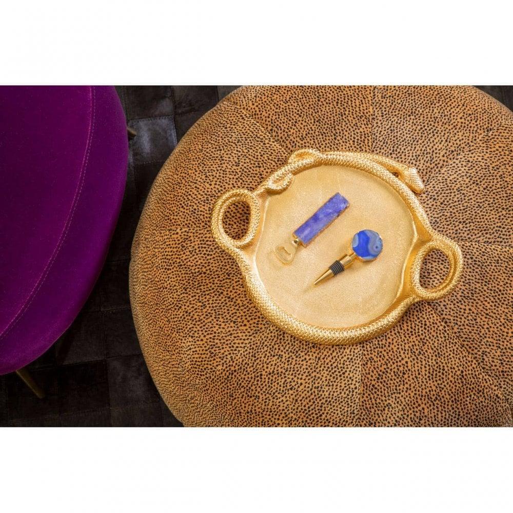 Gold decorative tray with bottle stopper and corkscrew on textured ottoman beside purple chair