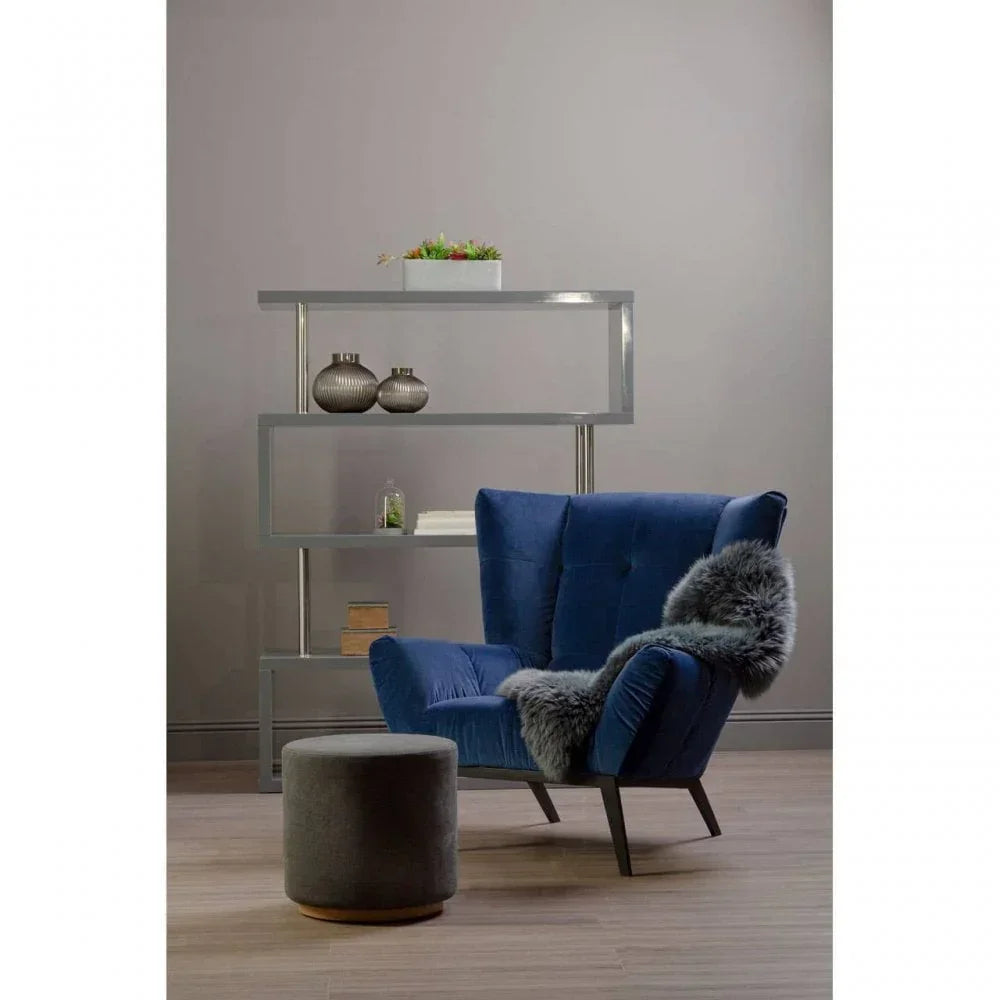 Blue velvet armchair with grey fur throw beside grey ottoman and modern shelving unit