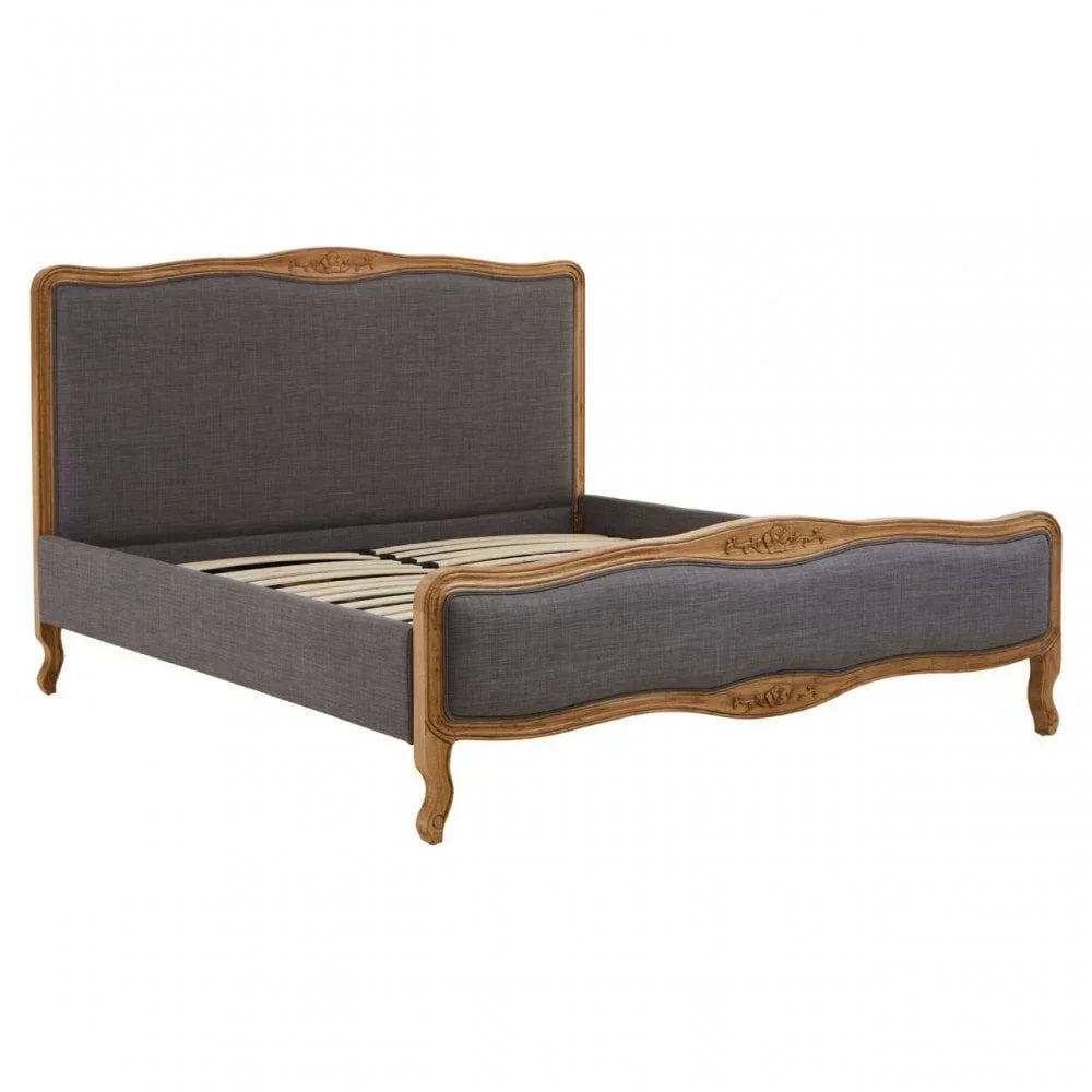 Grey upholstered wooden bed frame with carved headboard and footboard, angled front view