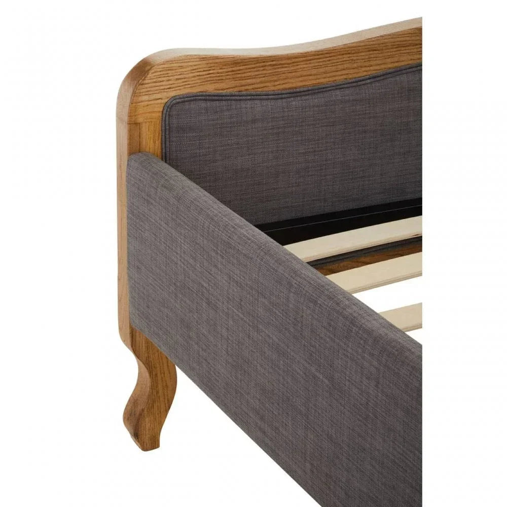 Grey upholstered bed frame with oak wood trim and curved leg