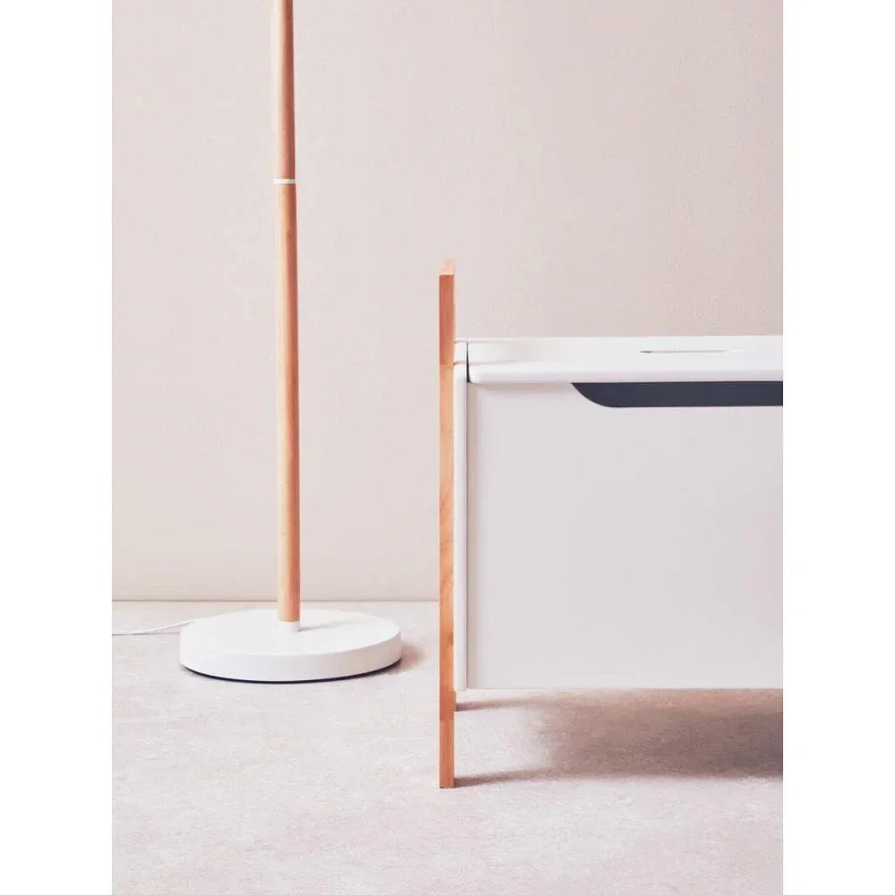 White storage bench with wood legs beside minimalist wooden floor lamp on carpet
