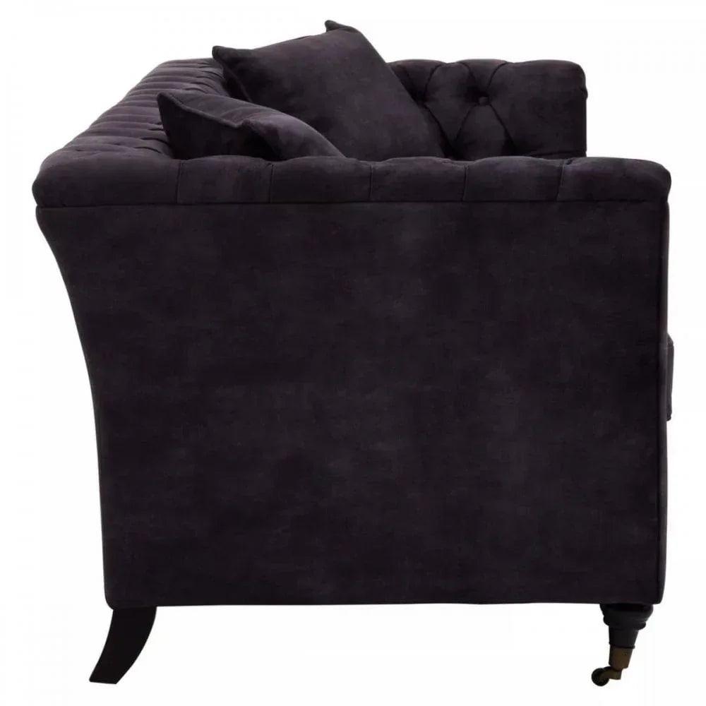 Side view of black velvet chesterfield sofa with tufted back and two matching cushions