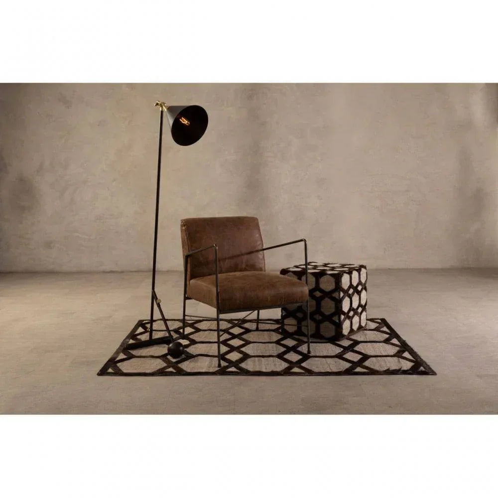 Brown leather accent chair with black metal frame on geometric rug beside cube ottoman and floor lamp