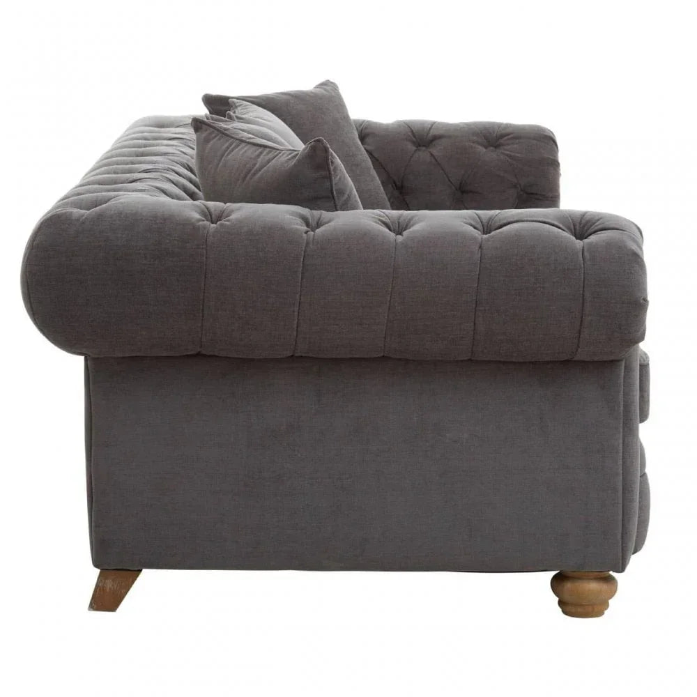 Side view of grey fabric sofa with deep button tufting and two matching scatter cushions