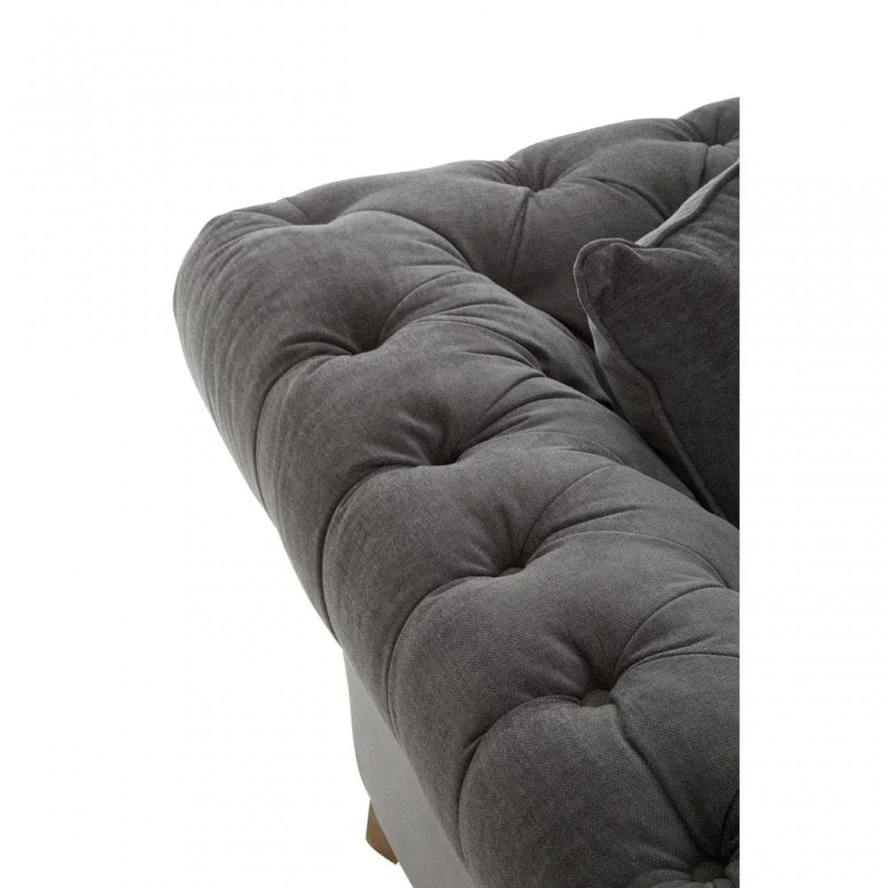 Close-up of grey fabric sofa with deep button tufting and plush armrest cushion