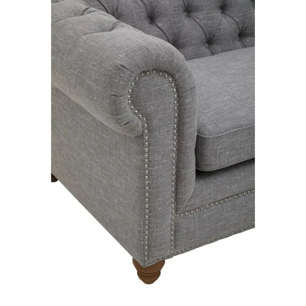 Grey fabric sofa arm with button tufting and silver stud detailing on wooden leg