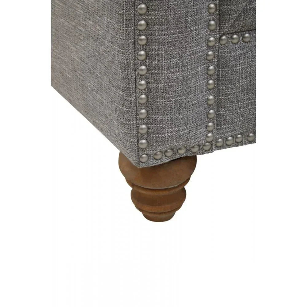 Grey fabric sofa corner with nailhead trim detail and turned wooden leg