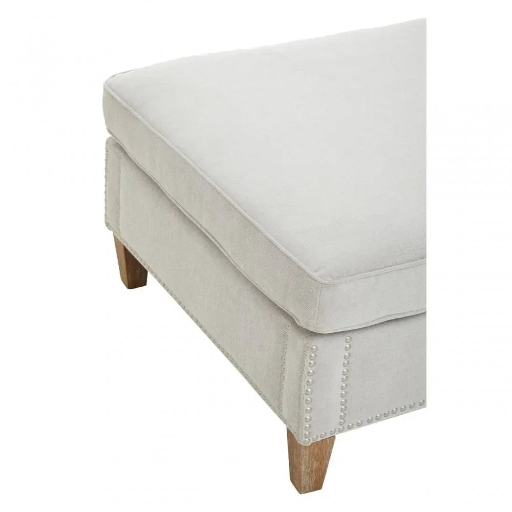 Light grey fabric ottoman with wooden legs and nailhead trim close-up