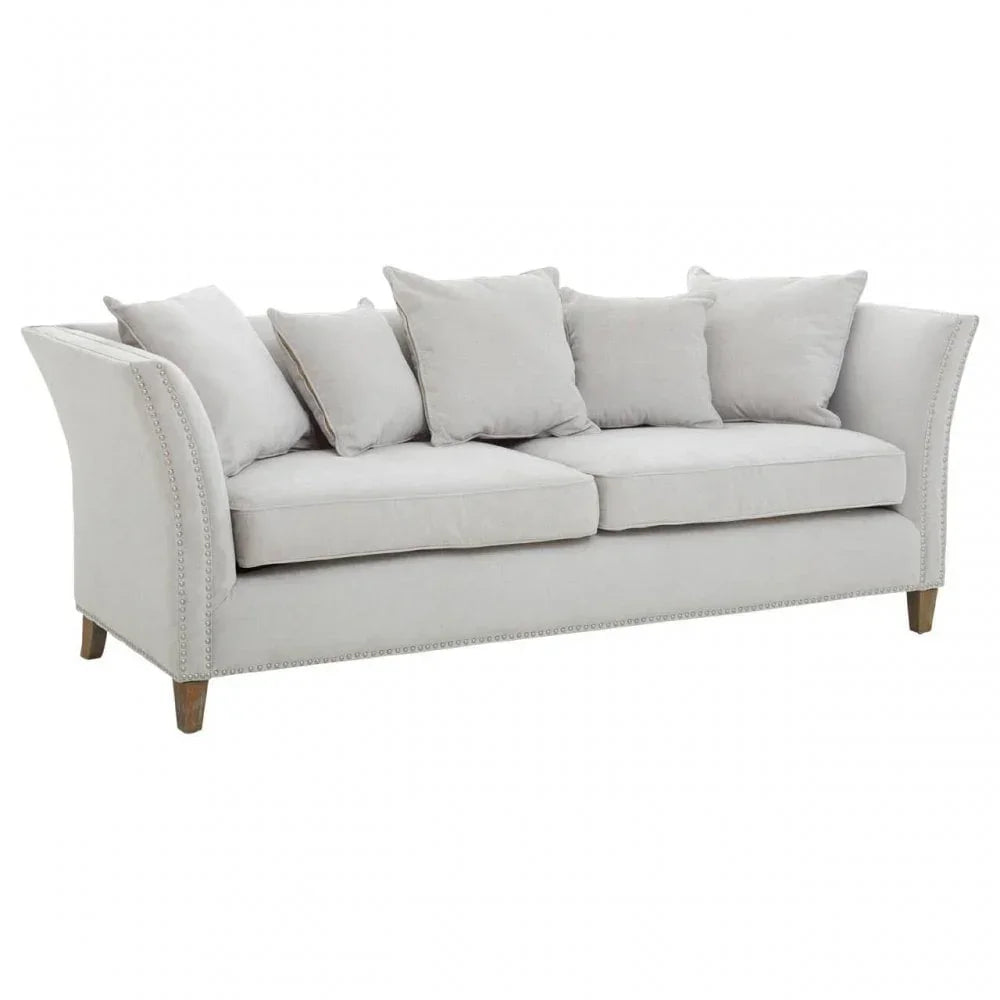 Light grey fabric sofa with studded arms and five scatter cushions on wooden legs