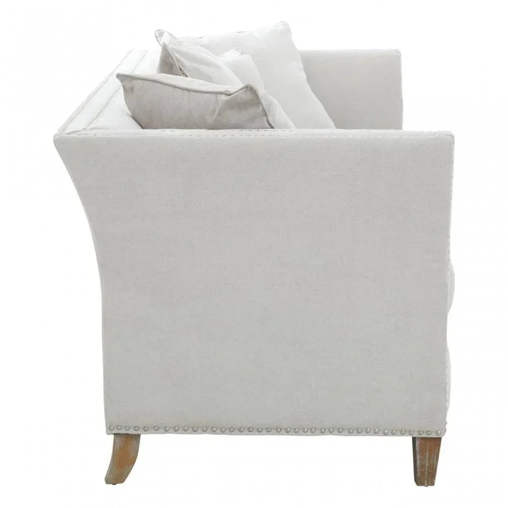 Side view of linen sofa with nailhead trim and wooden legs, neutral scatter cushions visible