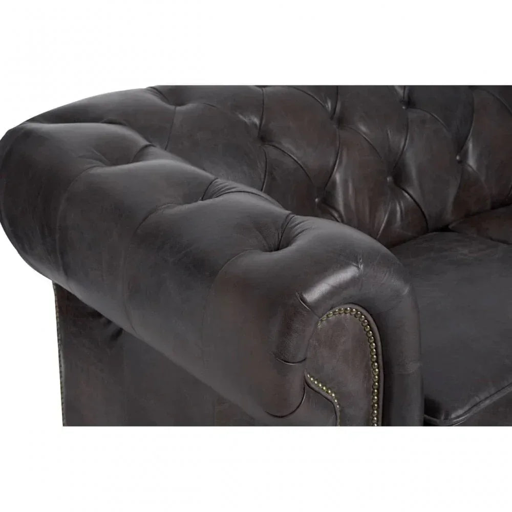 Close-up of brown leather sofa arm with button tufting and studded trim