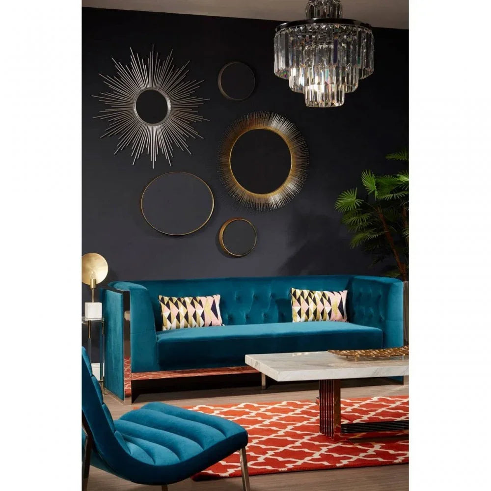 Teal velvet sofa with geometric cushions, marble coffee table, and sunburst wall mirrors