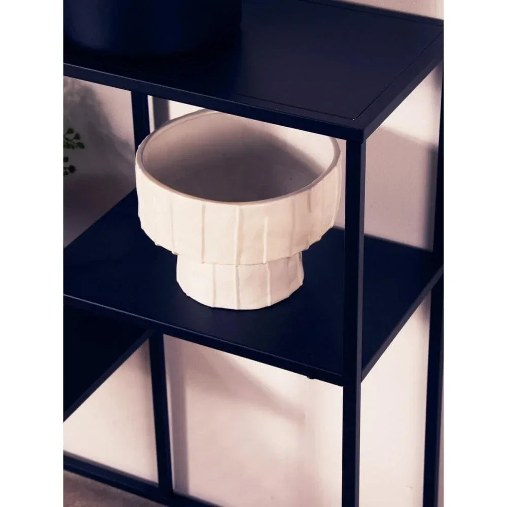 Cream ceramic bowl with textured design on black metal shelf