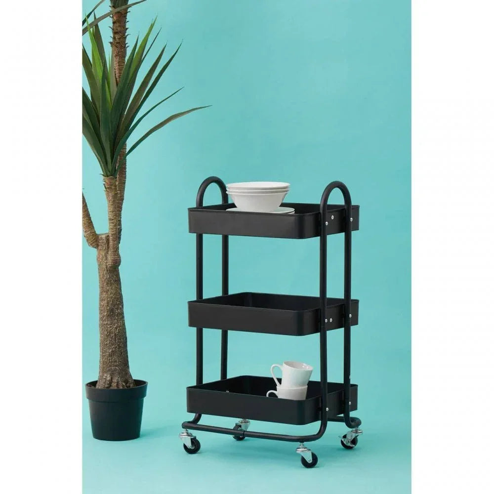 Black three tier metal storage trolley with dishes beside indoor plant on blue background