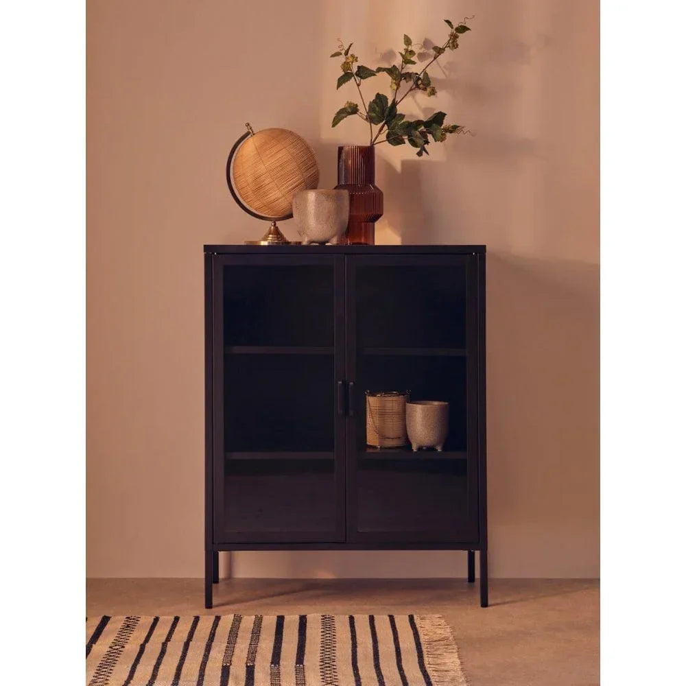 Black metal storage cabinet with glass doors, globe and vases on top, striped rug in front