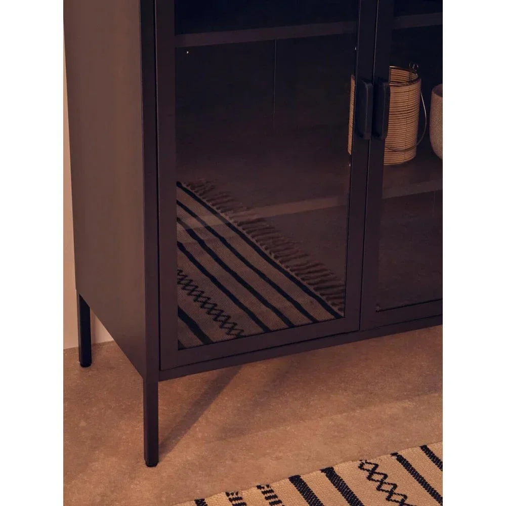 Black glass display cabinet with metal legs beside patterned rug on tile floor