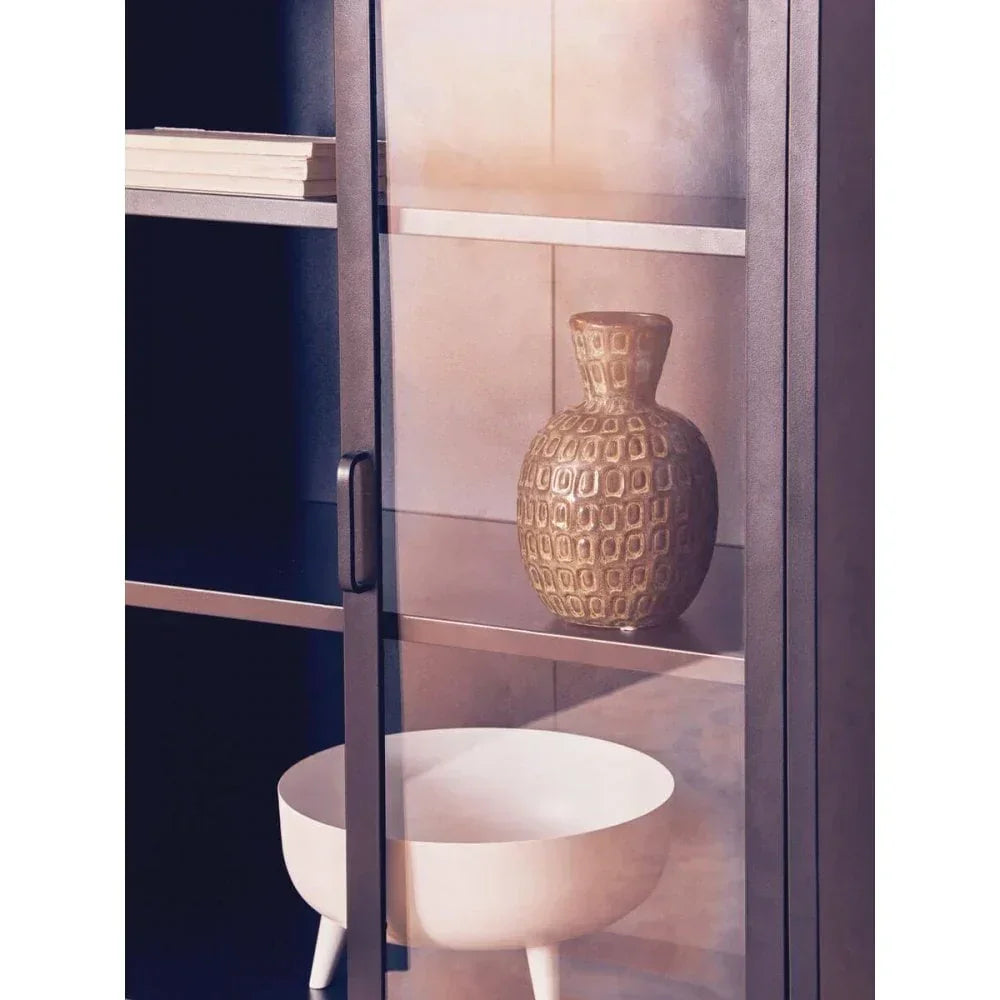 Metal display cabinet with glass door, ceramic vase, and white decorative bowl on shelves