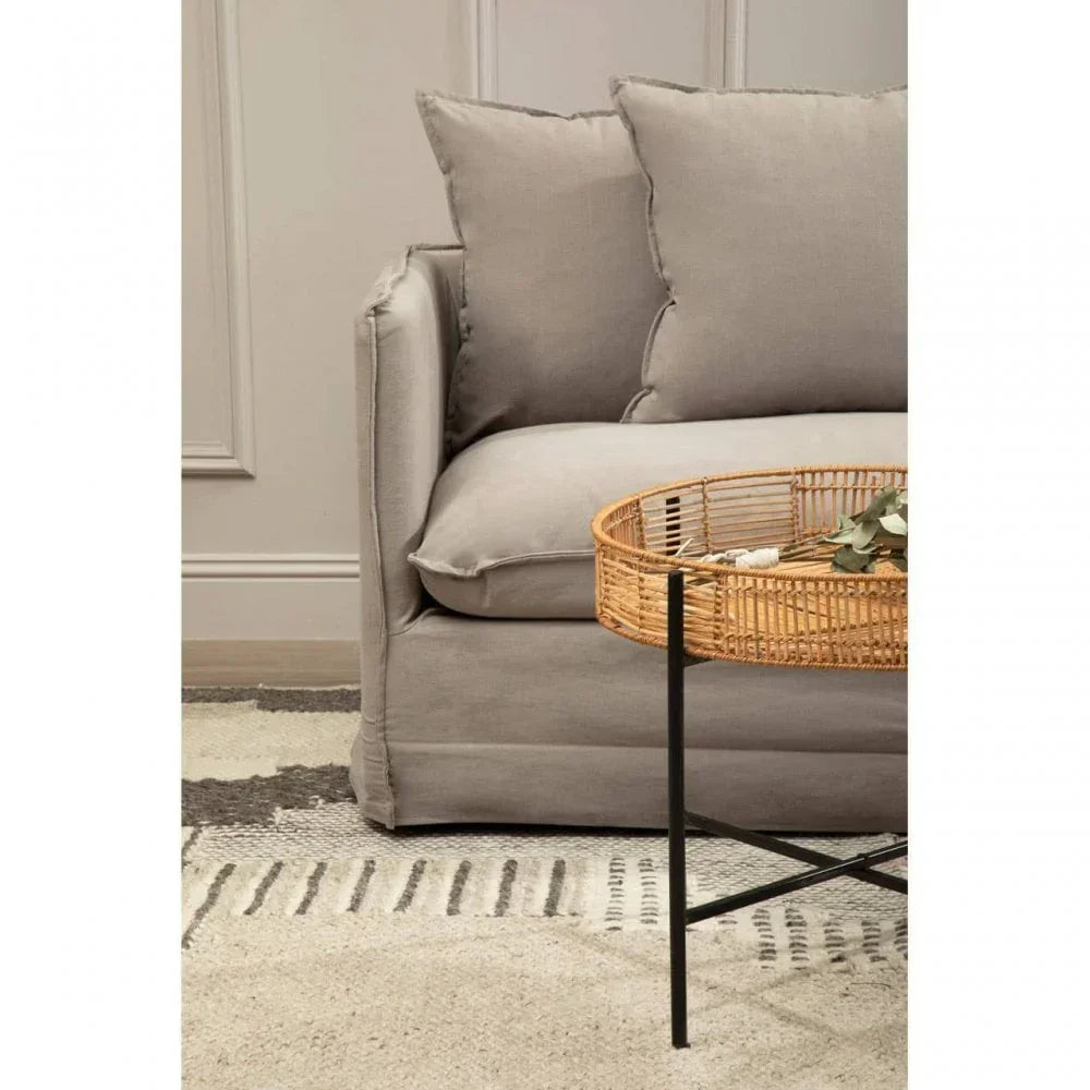 Light grey fabric sofa with scatter cushions beside round rattan coffee table on patterned rug