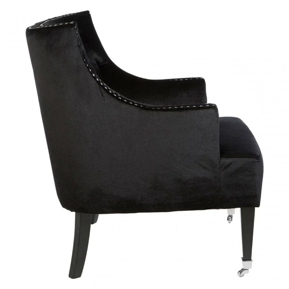 Black velvet accent chair with curved arms, silver stud detailing, and front caster legs