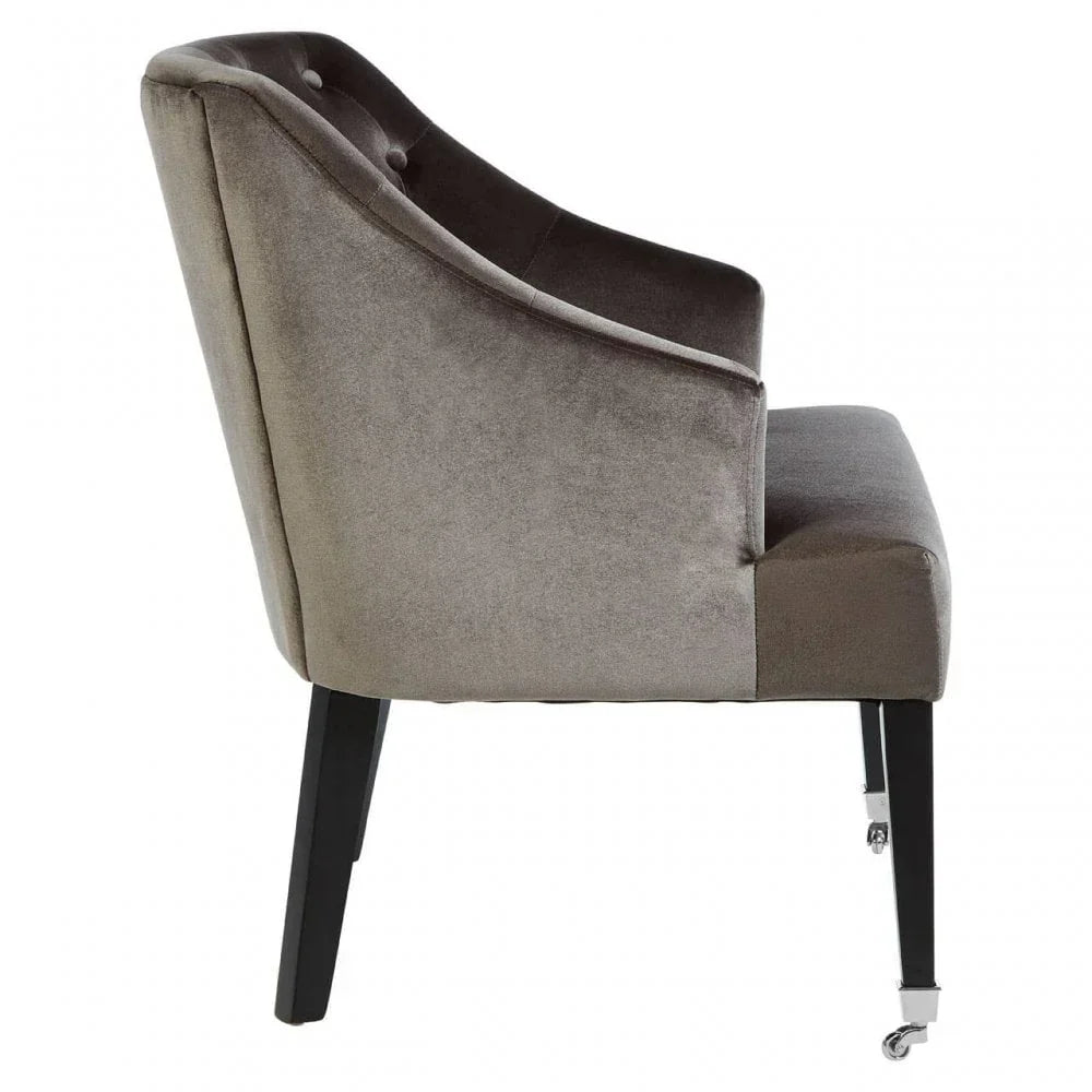 Grey velvet dining chair with black wooden legs and metal front castors, side profile view