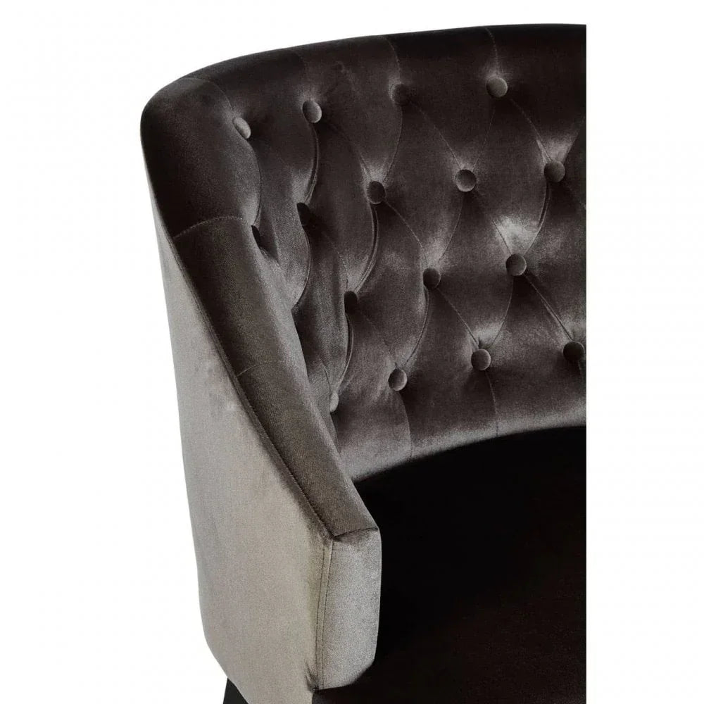 Close-up of dark velvet armchair with button-tufted backrest and curved arm