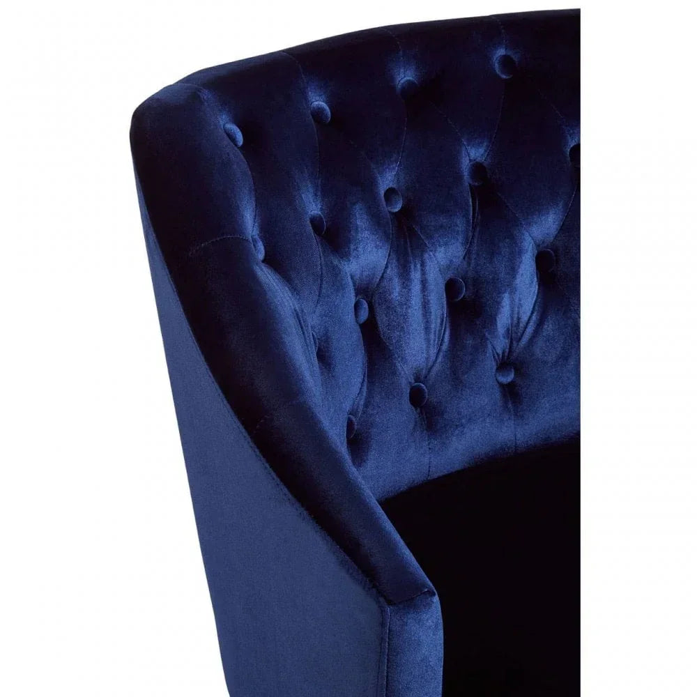 Closeup of blue velvet armchair with deep button tufted backrest and curved arm design