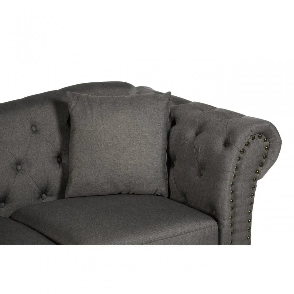 Dark grey fabric sofa corner with button-tufted back and brass studded rolled arm