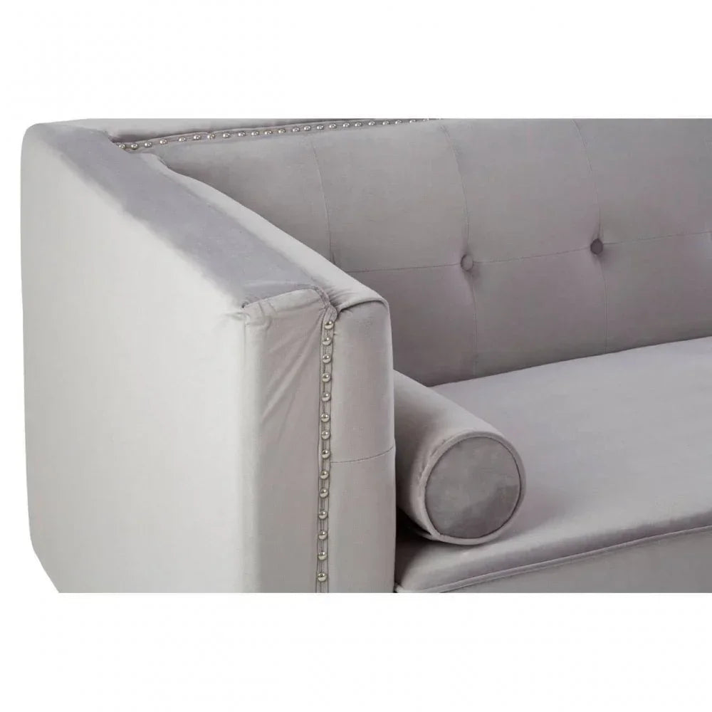Grey velvet sofa with tufted backrest, silver stud detailing and bolster cushion, angled view