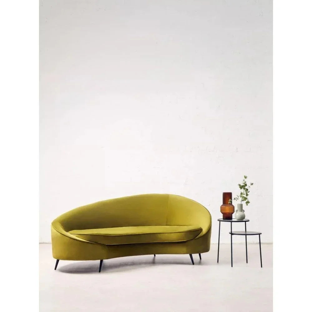 Olive green velvet sofa with black metal legs beside nested tables with vases and greenery