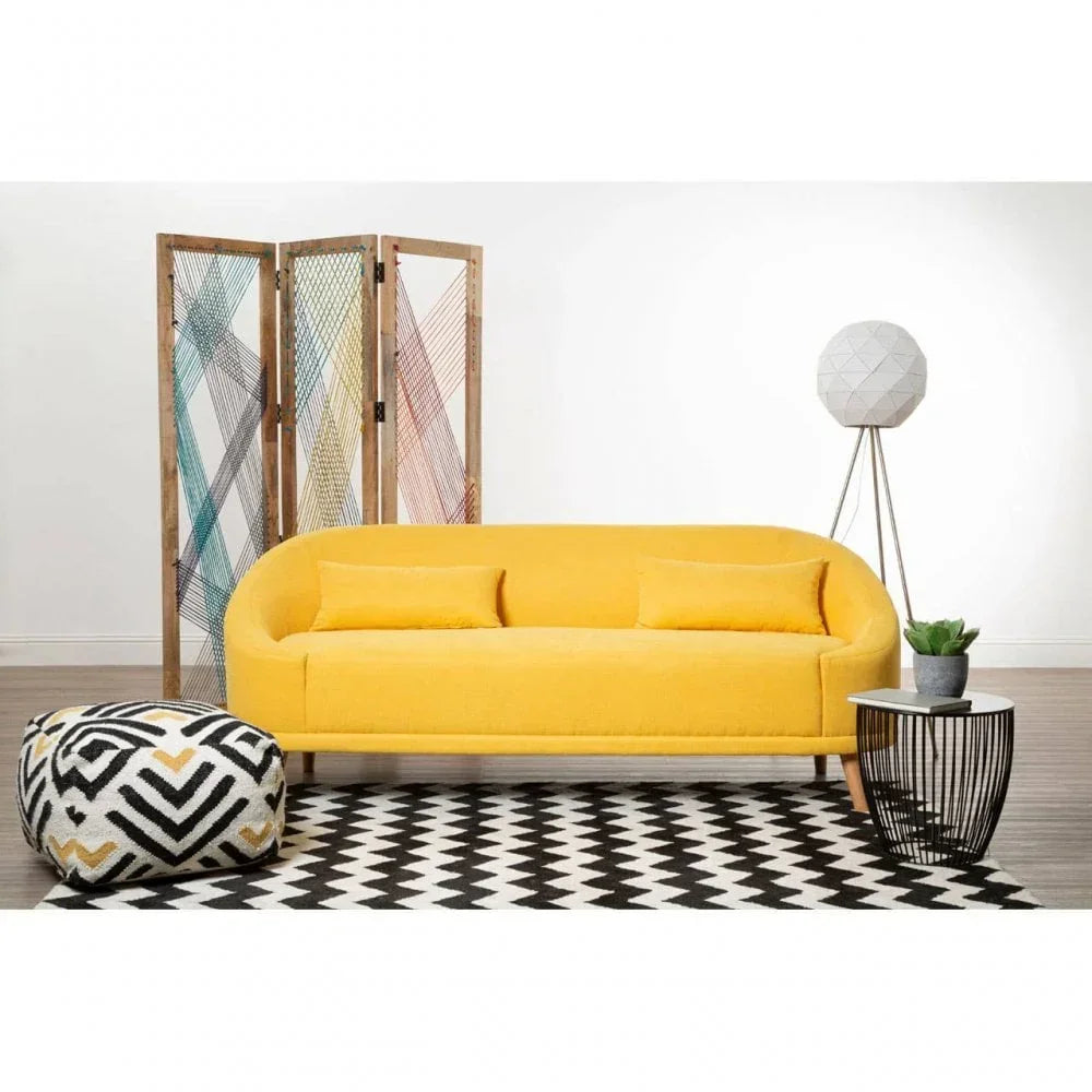 Yellow fabric sofa with two cushions, black and white pouffe, geometric rug, and side table