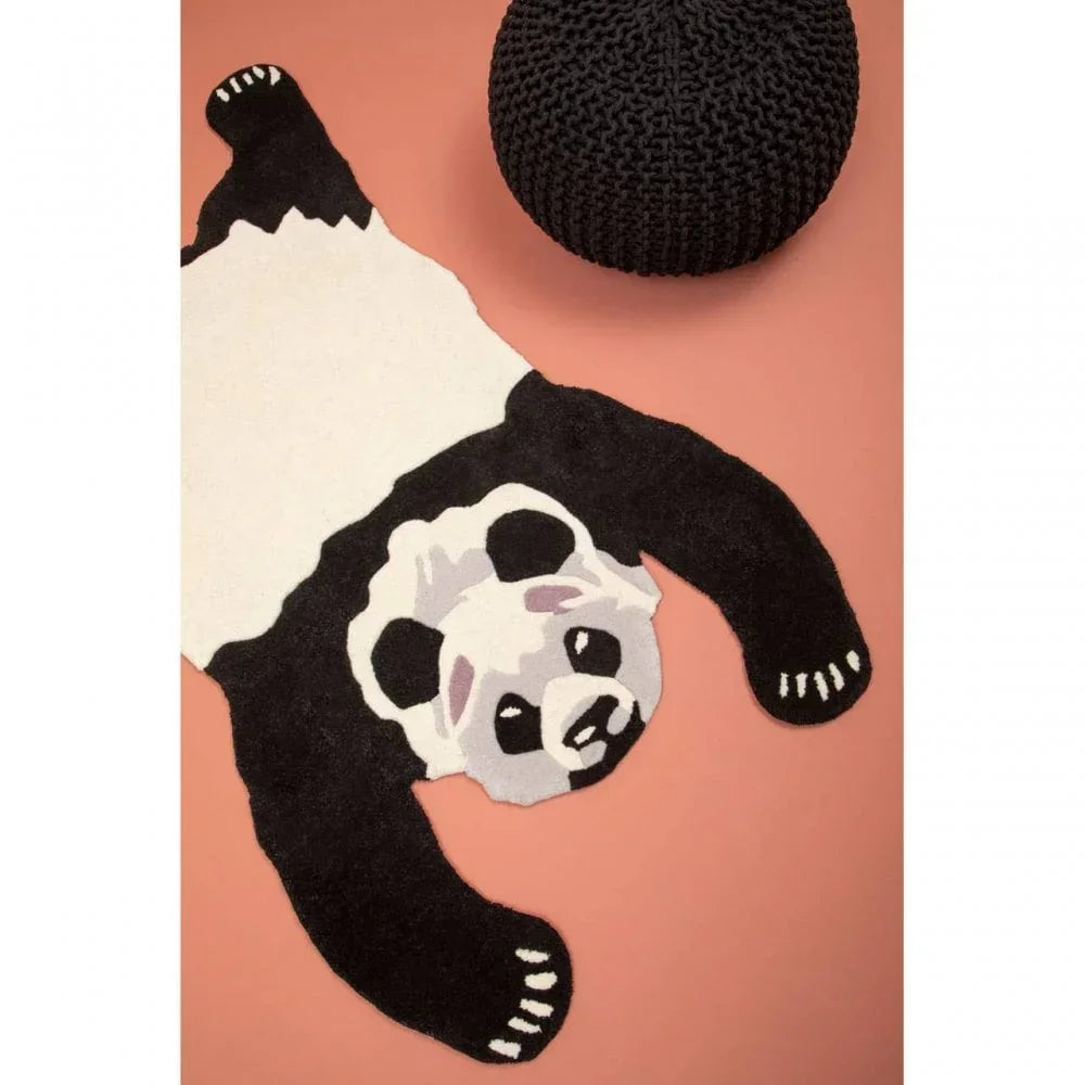 Panda-shaped rug on peach floor next to round black knitted pouffe