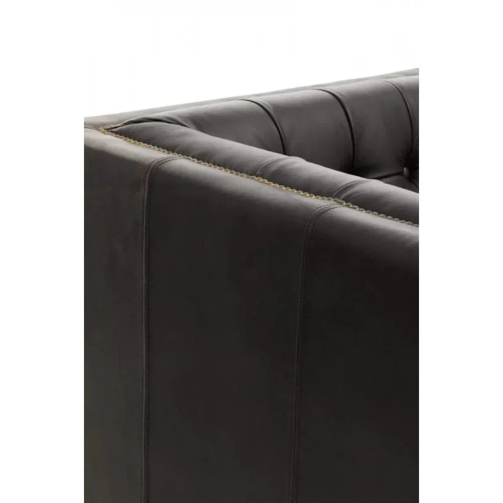 Close-up of dark leather sofa arm with stitched seams and brass nailhead trim