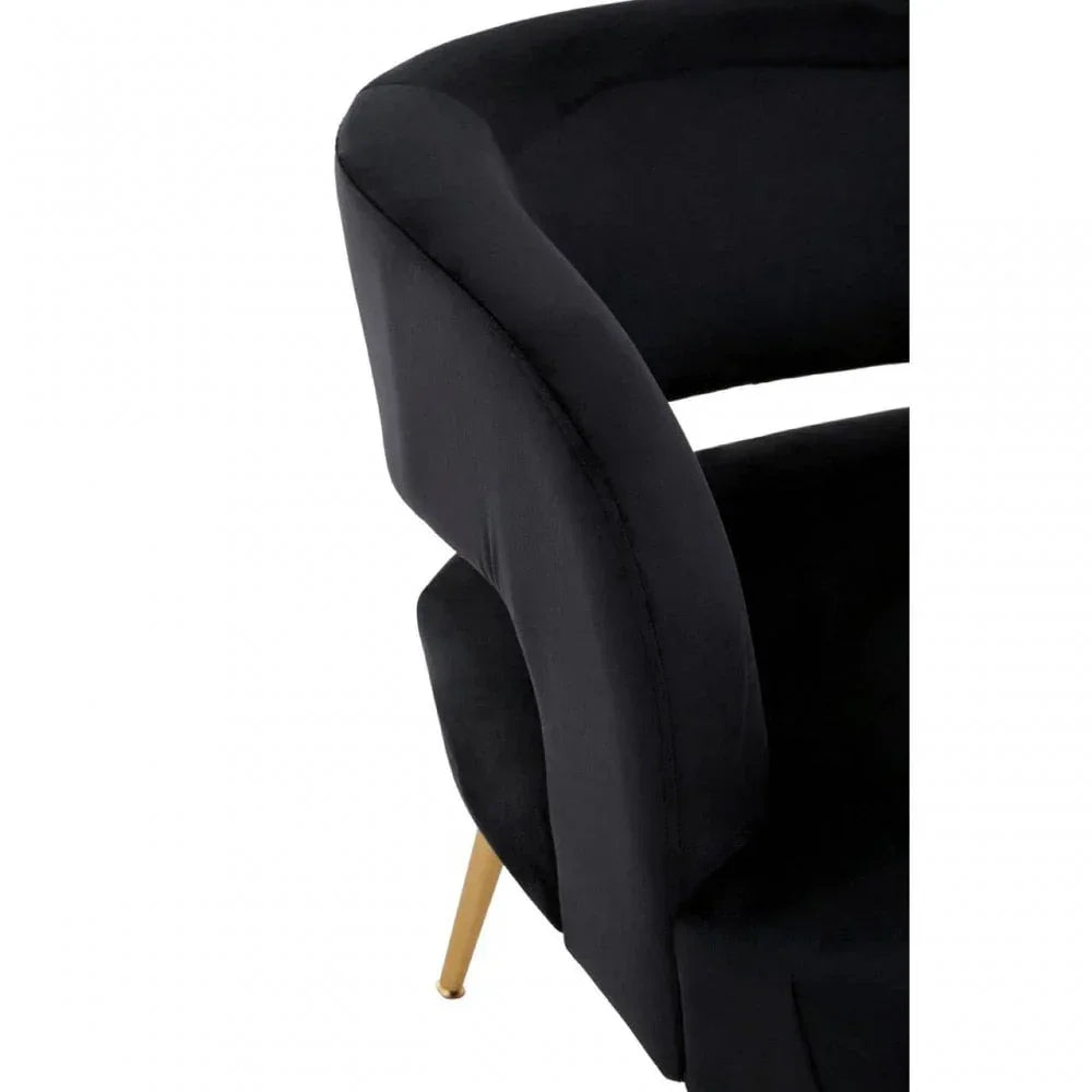 Black velvet accent chair with curved backrest and gold metal legs, close-up view