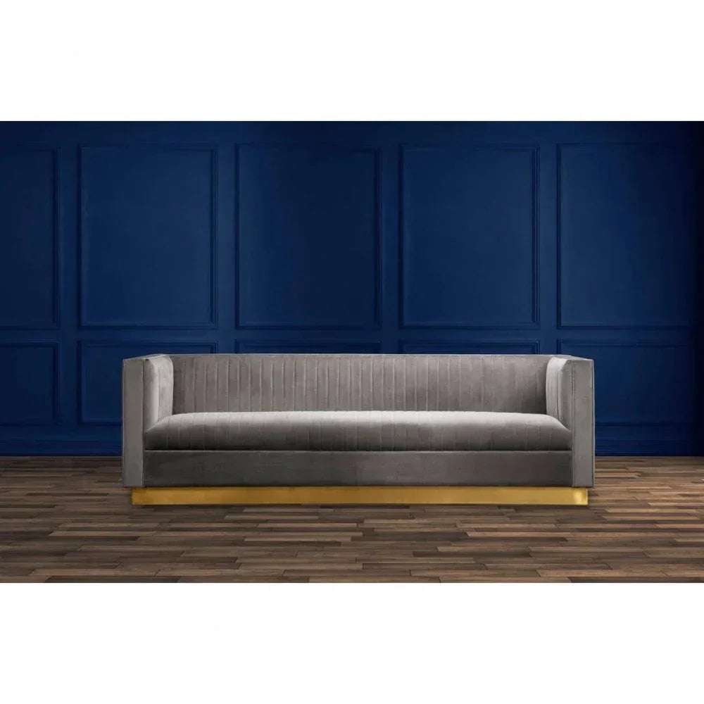Grey velvet sofa with gold base against blue panel wall and wooden floor